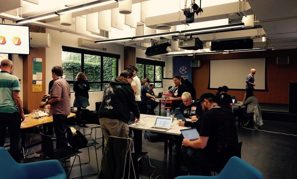 People standing around table one man in front with laptop on lap