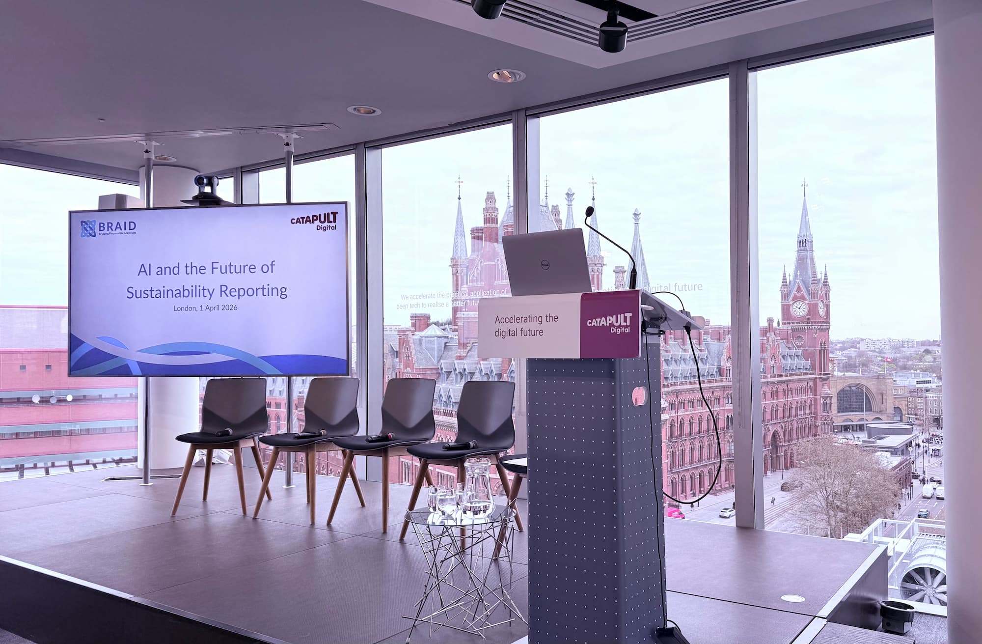 stage with screen showing event name, four chair and a lecturn, with st pancras visible through the windows