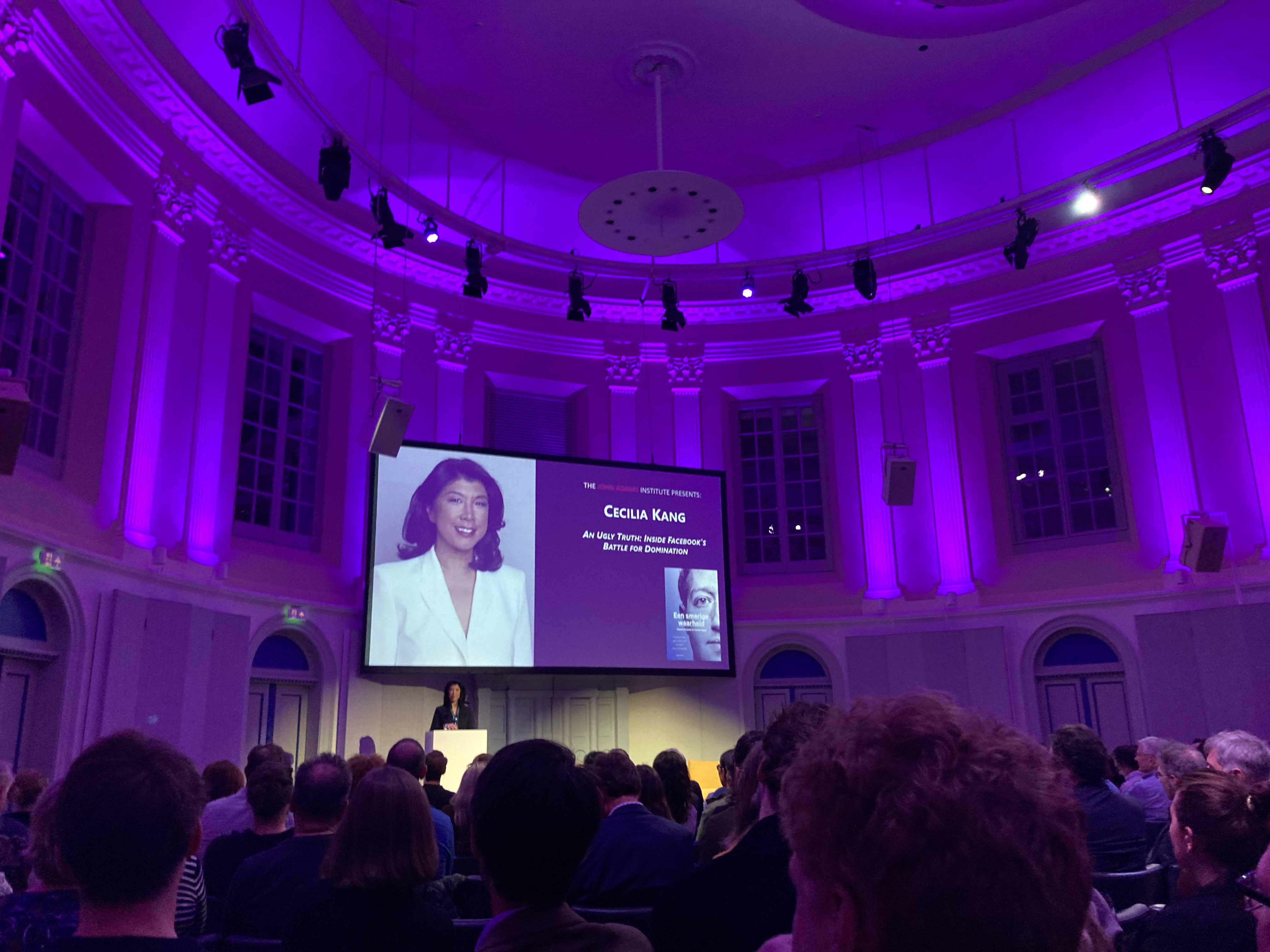 round conference hall with blue lights and cecilia kang on slide and on stage